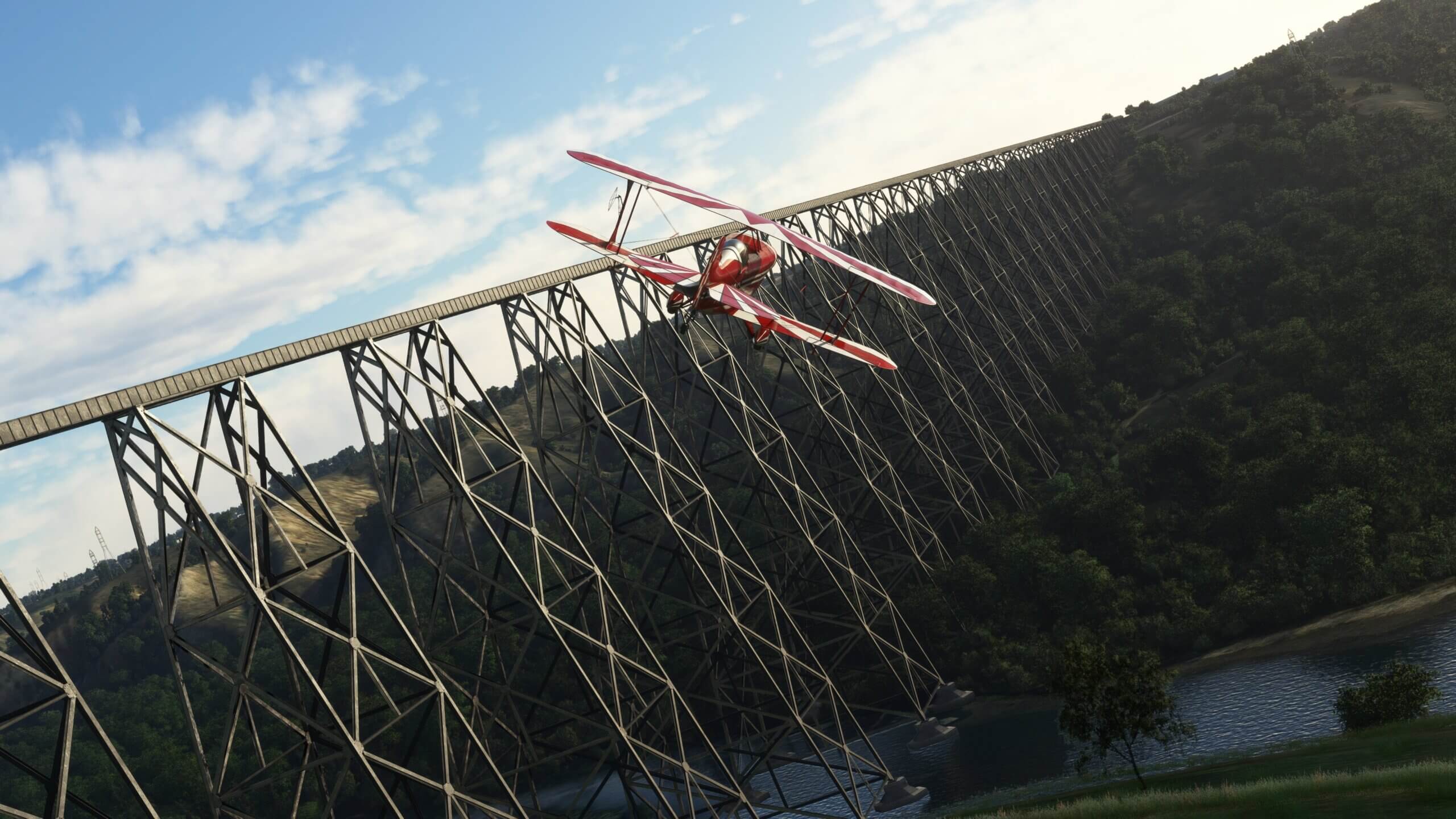 A dual wing red propeller aircraft banks right whilst flying alongside a tall bridge