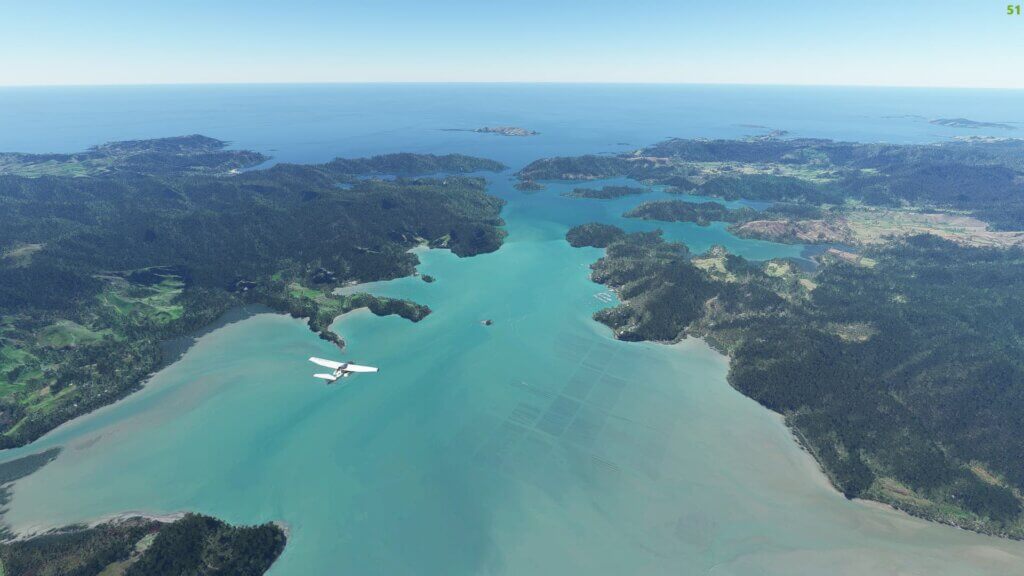 A single engine prop plane flies above an inlet of water with land on both sides